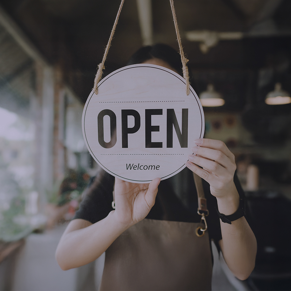 woman in apron turning open sign in a door