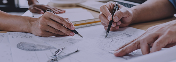2 peoples hands on a piece of paper that shows site plans - both have pens in their hands